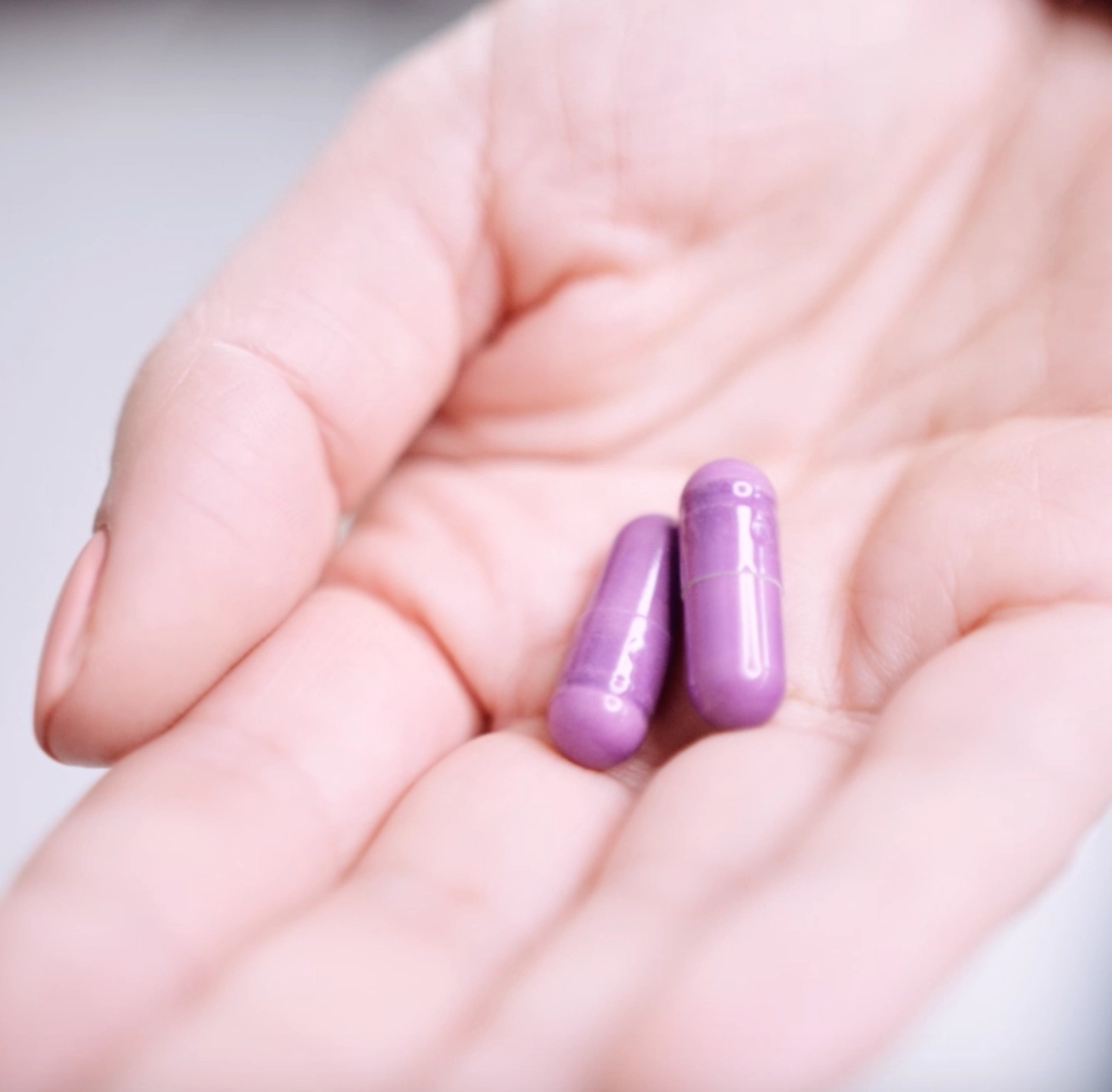 An open hand holding two purple capsules
