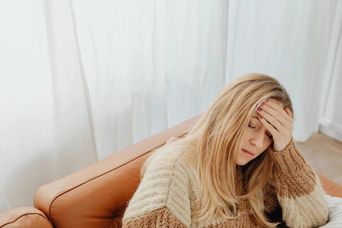 A woman sitting on a sofa with her hand on her forehead, looking tired